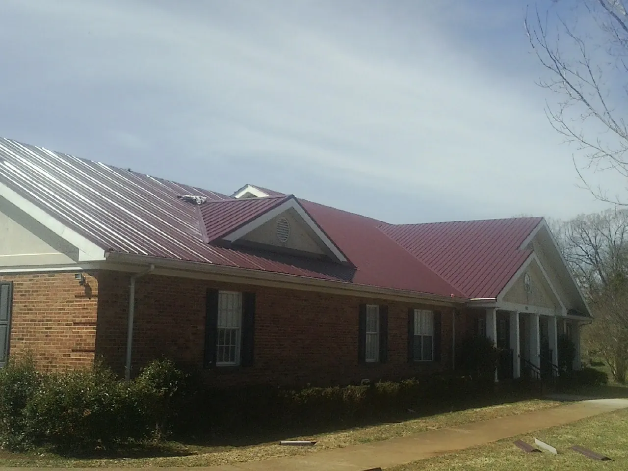 Red metal roof with gabled entries on a long brick building, from a Hail Damage Roof Repair job in Cottonwood